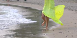美丽的年轻女孩的腿穿着长黄色的衣服赤脚跑在沙滩上的沙子靠近风微风海浪海岸快乐的假期旅游旅游度假女人旅行者享受自然