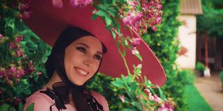 旧复古奥黛丽·赫本风格。粉红色的宽边帽子。自然化妆品概念，节日猫眼眼线化妆，可爱的脸性感的嘴唇。春天盛开的花园绿玫瑰丛中。时尚50 60年代