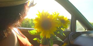 快乐的年轻旅行年轻女子享受公路旅行在夏天的自然与向日葵束。女孩挽着胳膊，把她的手伸出车窗，乘汽车旅行快乐的假期暑假