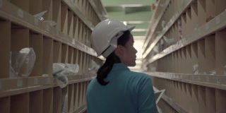 起重机跟随录像拍摄的亚洲女工人巡逻货物放在货架上的仓库