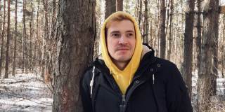一个年轻人在森林里散步的肖像。一个穿着黄色连帽衫和黑色夹克的帅哥在早春倚在树上摆姿势