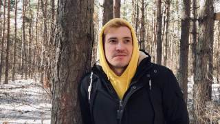 一个年轻人在森林里散步的肖像。一个穿着黄色连帽衫和黑色夹克的帅哥在早春倚在树上摆姿势视频素材模板下载