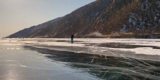 穿着蓝色裤子、戴着头盔、太阳镜、溜冰鞋和滑雪杖的酷男正在贝加尔湖的冰面上滚动。