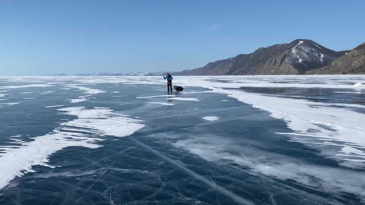 一个戴着头盔、穿着溜冰鞋、带着护膝、带着滑雪杖、背着背包的家伙正在贝加尔湖的冰面上打滚。