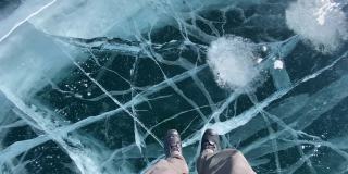 一个男人走在结冰的贝加尔湖上，湖面上有蓝色透明的冰，上面有很深的裂缝。