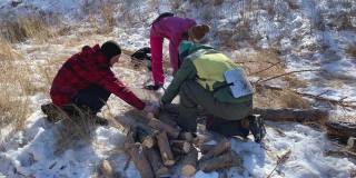 游客们正在用双手锯子锯木头。两个年轻人和一个女孩正在准备柴火。