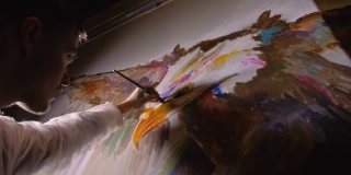 艺术家设计师在墙上画了一只鹰。工匠装饰用丙烯酸颜料画一幅画。画家穿着一件油漆外套。