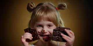 快乐微笑的小女孩吃着牛奶巧克力棒甜点孤立在黑暗的背景