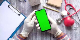 俯视图医生手在乳胶手套拿着智能手机与绿色屏幕