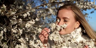 女孩在春天的树上触摸花朵的脸庞。浪漫的风格，女孩带着一朵花在公园里