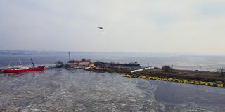 大型运输直升机飞过有人工海湾和停泊在融冰中的货船的运输港