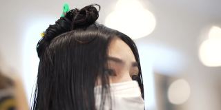 一个亚洲女人，她在美容院穿着护身衣，她卷头发，拉直头发。