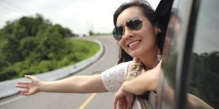 一个亚洲女人把她的手伸出车窗，笑了。慢动作
