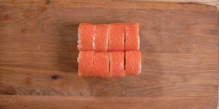在家里做寿司，男性将寿司卷放在切菜板上的特写镜头。