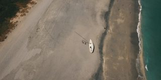 2021年3月春假和2019冠状病毒病期间，佛罗里达州朱诺海滩海滩海岸线上的一艘废弃帆船的动态鸟瞰图