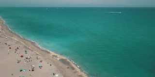 2021年3月春假和新冠肺炎期间，佛罗里达州朱诺海滩海滩海岸线上的彩色沙滩伞和人们的动态鸟瞰图