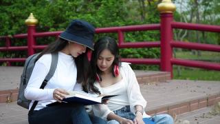 两个女大学生坐在校园里看书。视频素材模板下载