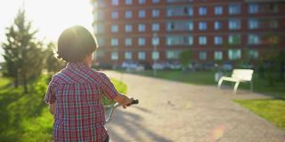 在夏日阳光明媚的夕阳下，一个小男孩在马路上骑自行车。快乐的男孩骑着自行车，在户外享受大自然的乐趣。积极运动快乐家庭休闲度假。慢动作