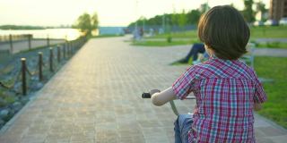 在夏日阳光明媚的夕阳下，一个小男孩在马路上骑自行车。快乐的男孩骑着自行车，在户外享受大自然的乐趣。积极运动快乐家庭休闲度假。慢动作