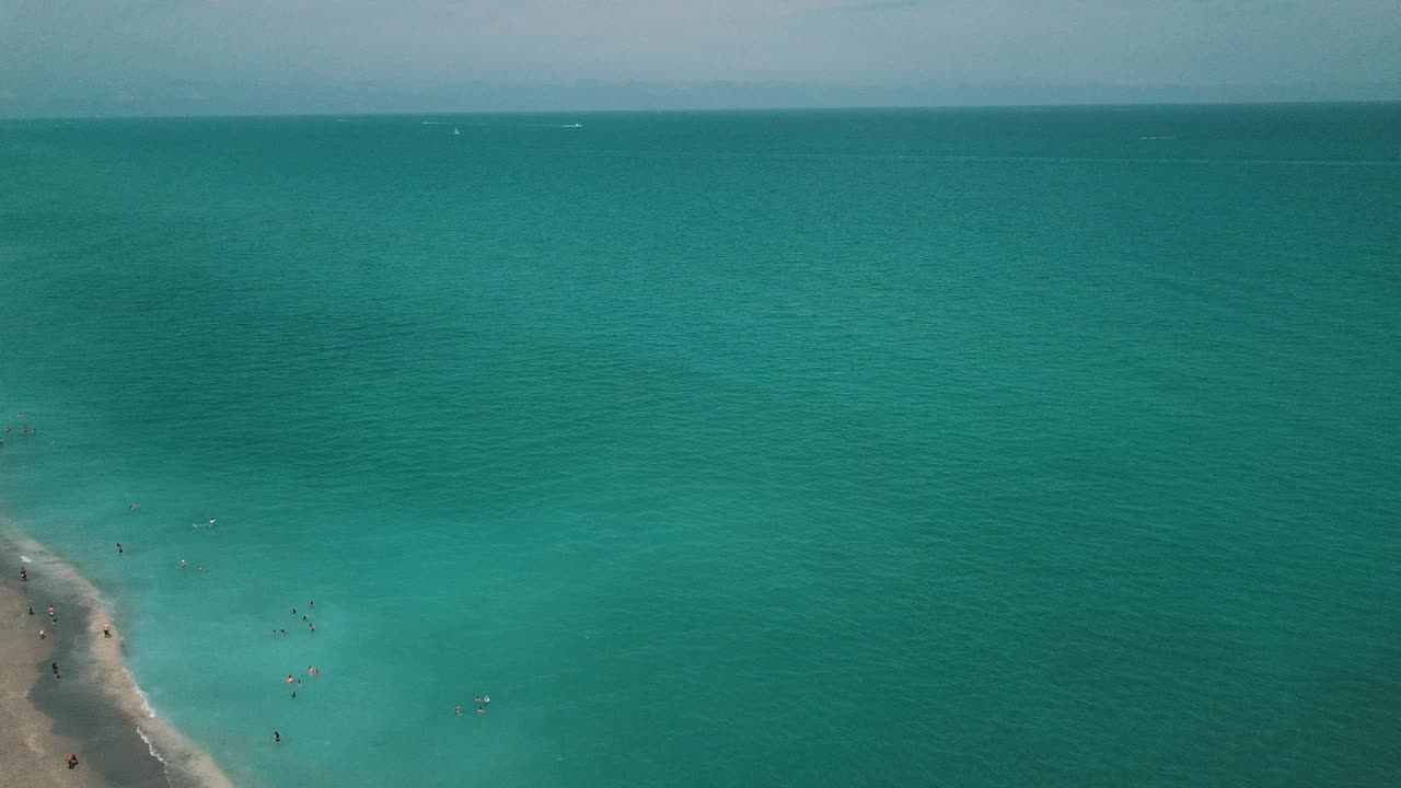 2021年3月春假和COVID-19期间，佛罗里达朱诺海滩正午沙滩上彩色沙滩伞和人们的动态鸟瞰图