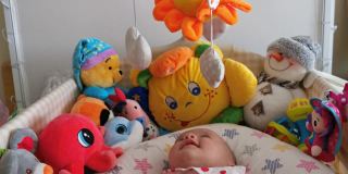 微笑的婴儿看着她的玩具，笑着看着玩具旋转。三个月大的女婴在床上玩耍。COVID-19大流行期间的新生儿。