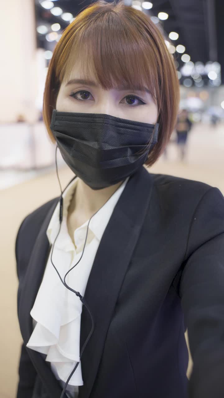 垂直视频美丽的亚洲商务女性戴面具视频Calling在展览活动