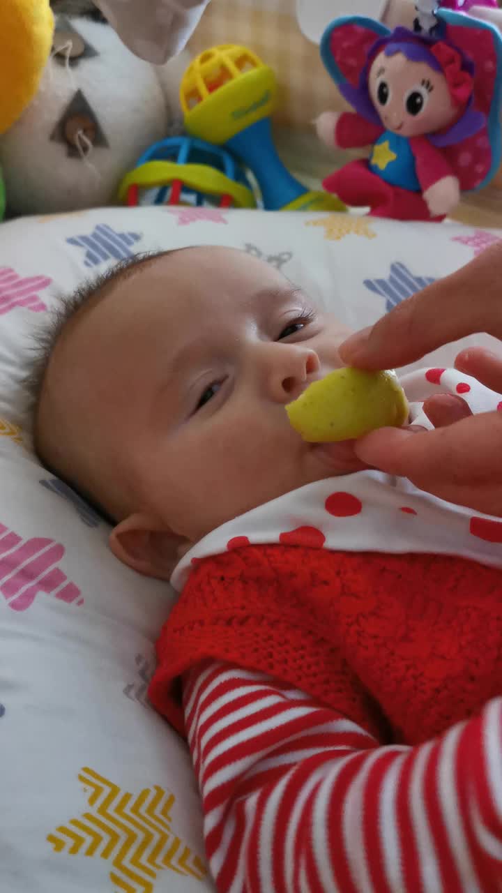 宝宝在吃苹果。三个月大的宝宝吃水果早餐。寻找快乐。