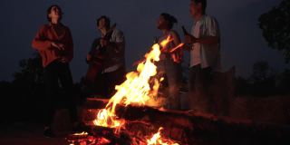 朋友们在野外露营时，在火边跳舞、弹吉他。