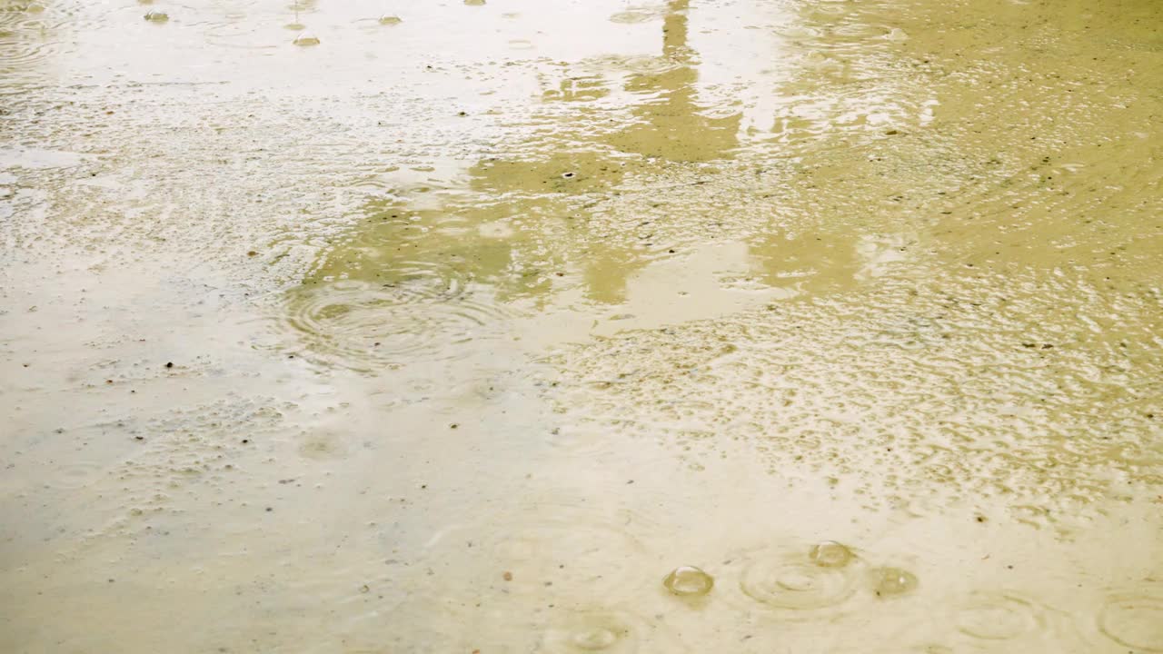 大雨滴落在潮湿的沥青表面的特写。潮湿的水坑和水泡