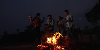 朋友们在野外露营时，在火边跳舞、弹吉他。