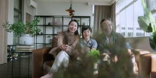 幸福快乐的亚洲家庭父母和儿子儿子一起看电视，在客厅的沙发上度过假期的周末时间。家庭和家庭的概念。