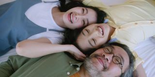 幸福快乐的亚洲家庭妈妈爸爸和可爱的儿子孩子躺在卧室白色柔软的床上笑着放松休闲的周末活动，俯视图手持拍摄慢镜头