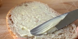 在面包上涂黄油。慢动作刀在面包表面涂黄油。特写镜头