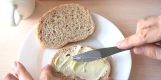 在面包上涂黄油。慢动作刀在面包表面涂黄油。特写镜头