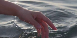 一个女人的手的特写是轻轻触摸海面上的海浪在日落