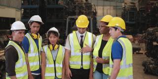 仓库里一群穿着制服、戴着头盔的人:不同种族的工人，如白种人、黑人和亚洲人，是工厂的员工和同事，在公司里合作和和谐。