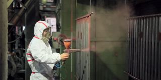 金属零件粉末喷涂。穿着防护服的工人用枪在金属制品上喷涂粉末涂料