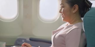 亚洲资深商务女性乘客在飞机上独自坐在商务舱感觉放松，享受和快乐喝一杯咖啡。旅游旅游度假或假日概念。