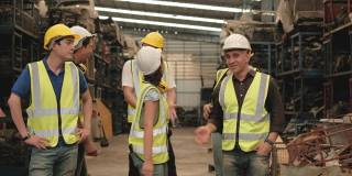 各种族的工人和工程师在机器零件仓库的休息时间开玩笑。整个团队都穿着安全制服和头盔。