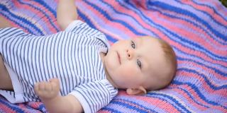 一个漂亮的蓝眼睛的小孩躺在彩色的毯子上。