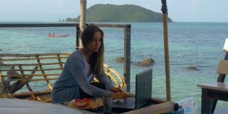 商务女性在一个美丽的热带岛屿上用笔记本电脑工作