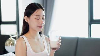 喝牛奶的亚洲年轻女子。早上下班之前。视频素材模板下载