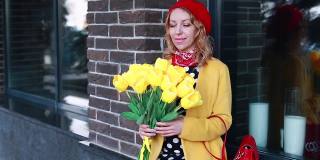 一个金发碧眼的白人女孩，穿着一件带有圆点图案的裙子，一件黄色的外套，戴着一顶红色的贝雷帽，坐在外面一栋建筑的窗台上欣赏着一束黄色的郁金香