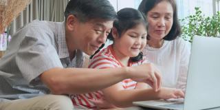 姥姥姥爷教小孙女用笔记本电脑坐在沙发上，幸福的关系纽带一代亚洲家庭花时间在家里一起玩笔记本电脑
