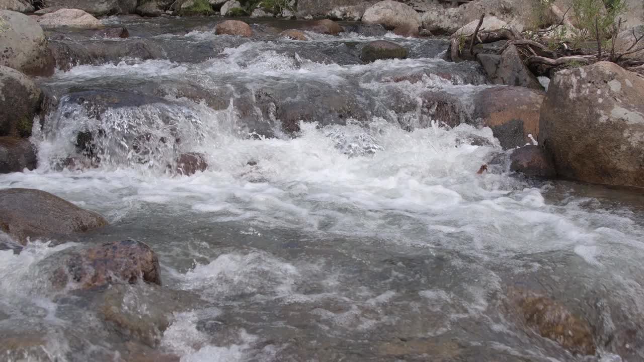 山间的河水从巨石上奔流而下。湍急的水流搅动水流，溅起水花。石质河床。透过透明的表面可以看到花岗岩底部