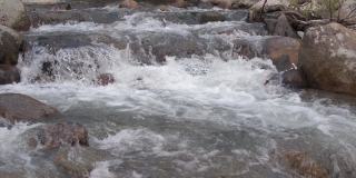 山间的河水从巨石上奔流而下。湍急的水流搅动水流，溅起水花。石质河床。透过透明的表面可以看到花岗岩底部