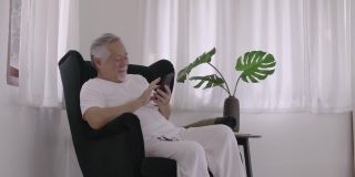 亚洲老人在房间里玩智能手机。