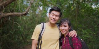 年轻的亚洲男人和女人的朋友一起在森林里旅行的肖像。情侣们在大自然中感到清新和放松，站在一起拥抱。然后微笑着看着镜头。