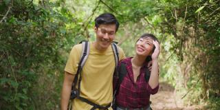 年轻的亚洲男人和女人朋友一起在森林里旅行。情侣们在大自然中感受清新和放松，一边看一边指着风景，然后一边拥抱和幸福地走着