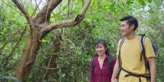年轻的亚洲男人和女人朋友一起在森林里旅行。情侣们在大自然中感受清新和放松，看着窗外的风景，然后带着幸福和乐趣继续散步。